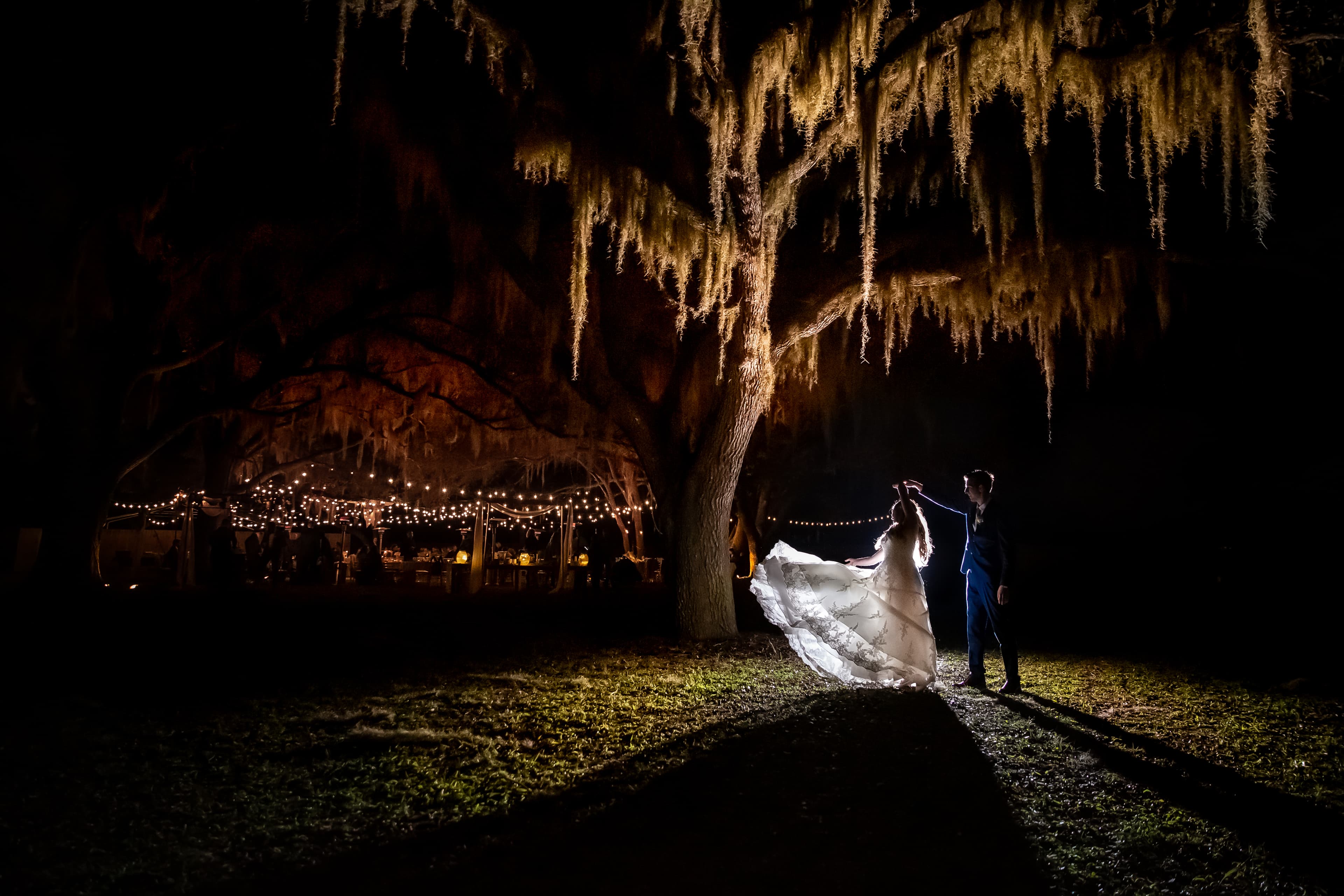 A couple dancing under moss-draped oaks strung with market lights at Chapel Creek